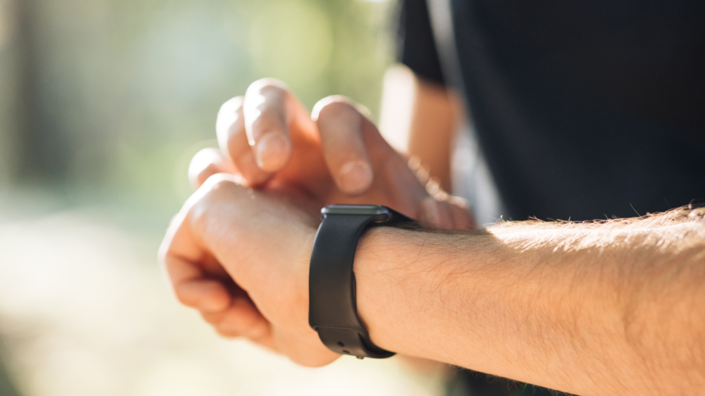 Das Bild zeigt eine männliche Person mit einem schwarzen T-shirt. Er tippt auf seiner Smartwatch herum. Smartwatches können die Herzratenvariabilität (HRV) messen. Deswegen steht das Bild symbolisch für die Herzratenvariabilität. Das Bild wird für einen Beitrag genutzt in dem es um die Herzratenvariabilität geht und warum diese für Personen mit CED wichtig ist.